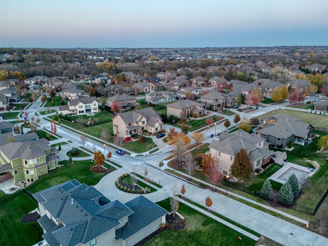 An aerial photograph of Silverleaf Estates captures a sprawling suburban neighborhood in Elkhorn, NE, featuring rows of single-family homes with manicured lawns and winding streets. The scene is set during twilight, with autumn-colored trees scattered throughout the landscape.